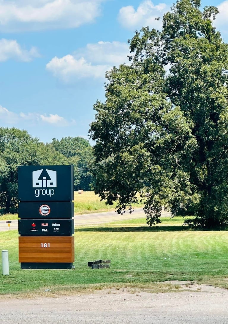 A business sign for group displaying the number 181 stands in a green field with large trees