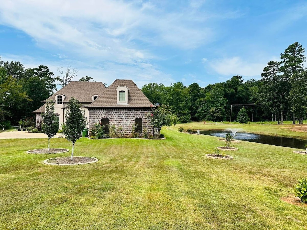 Stone mansion with mansard roof on expansive manicured lawn beside water feature