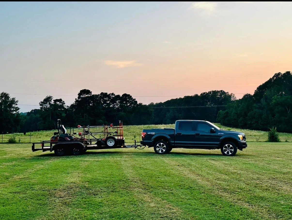 Blue pickup truck towing a farm trailer in an open green field at sunset